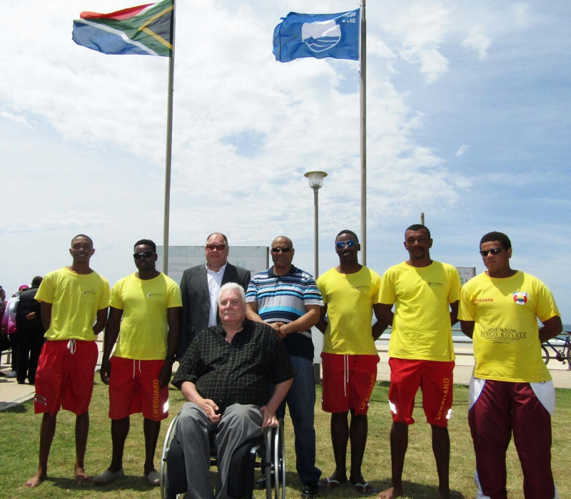 Finance Portfolio Councillor Brenton Williams (third left, standing), Social Services Portfolio Councillor Danny Benson (fourth left, standing), Jakkie Pieters of the Association of People with Disabilities and the Dolphin Beach lifeguards at the hoisting of the Blue Flag on Friday.